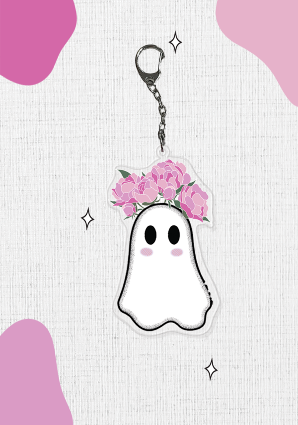 Introducing the Jood Ghost Keychain: a charming accessory showcasing an adorable ghost with rosy cheeks and pink flowers growing from their head. The background boasts abstract pink shapes and scattered sparkles, adding a whimsical and playful touch.