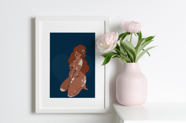 Framed artwork of a voluptuous woman with vitiligo on a dark blue background next to a vase with pink peonies.