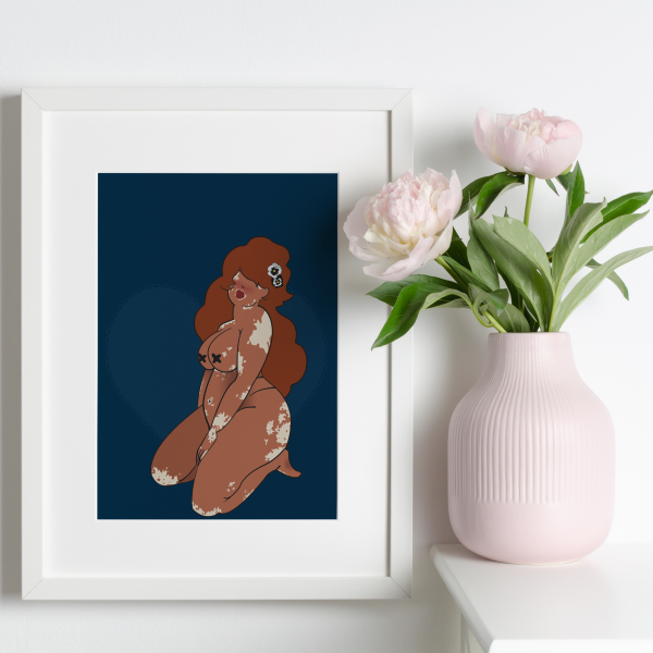 Framed artwork of a voluptuous woman with vitiligo on a dark blue background next to a vase with pink peonies.