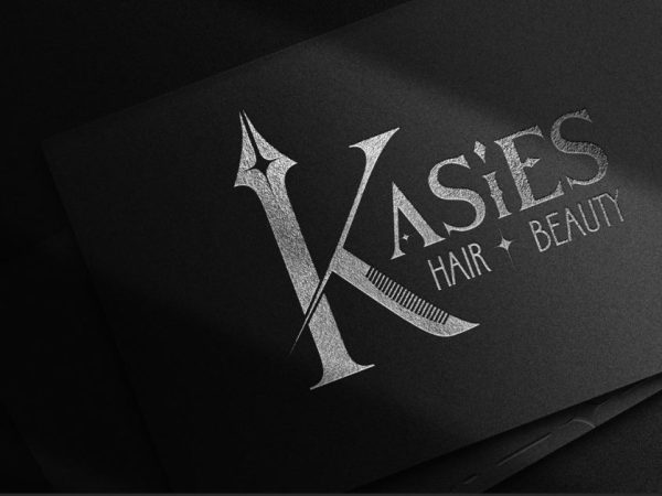 A black card with silver metallic text that reads "Kasie's Hair + Beauty" with a large stylized letter "K" on the left side. The background is shadowy and dark, allowing the text to stand out prominently.